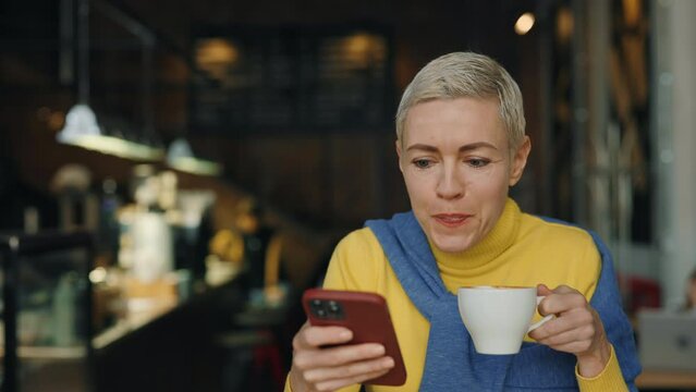 Middle aged caucasian blonde with coffee and mobile at cafe