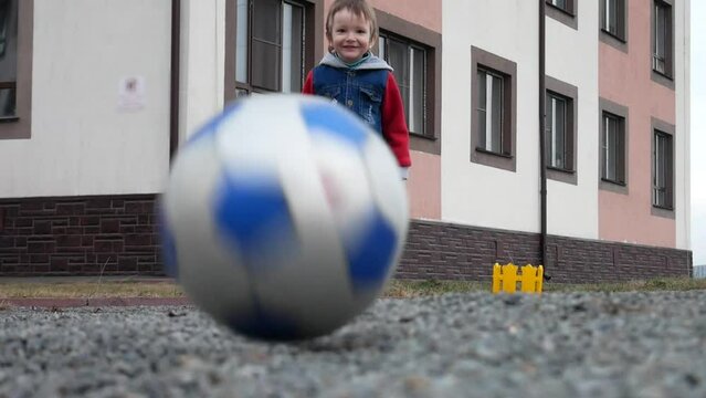 A cute happy boy kicks the ball into a camera on the ground