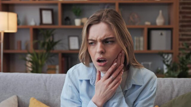 Toothache. Unhappy young woman touch cheek, suffers from toothache, girl having terrible sudden tooth pain, need dental treatment, sitting on sofa at home Medical insurance Tooth disease concept.