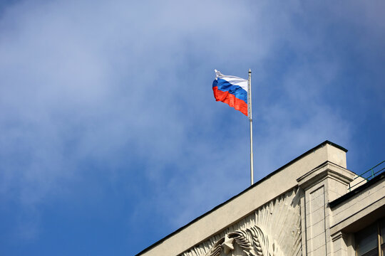 Russian flag on the parliament building in Moscow on background of blue sky and white clouds, authority of Russia