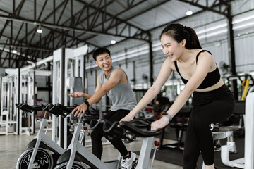 Fototapeta na wymiar exercise concept The well-shaped lady and the muscular man being entertaining having small chat while riding the exercise bike machines