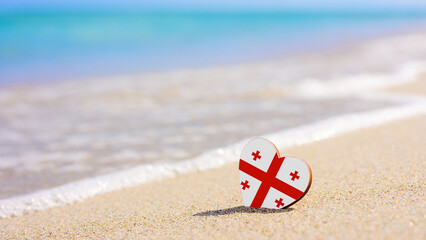 Flag of Georgia in the shape of a heart on a sandy beach. The concept of the best vacation in Georgia resorts