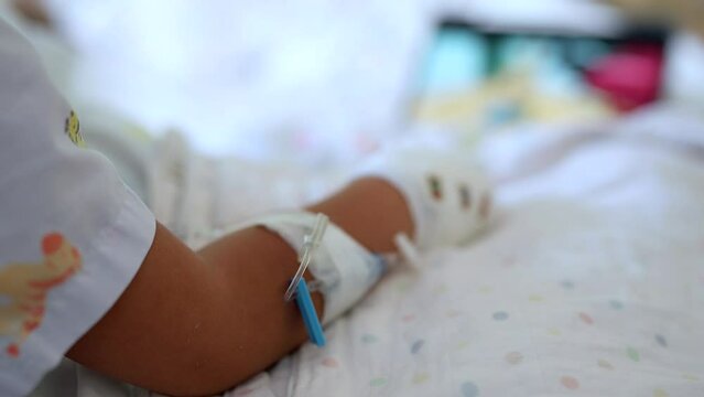 Close up child's hands twith Iv Infusion sitting on bed watching tablet.