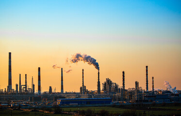 Fototapeta premium Working oil refinery. Smoke from the factory chimney. Ecological pollution. Air emissions polluting the city. Industrial waste is hazardous to health. Large factory in smog, Production in operation.