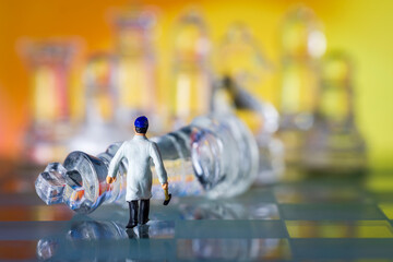 Glass chess board and pieces. Miniature man with hammer walking towards fallen king warm background macro