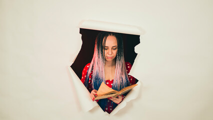 Young woman reading book in hole of white background in studio. Pretty female flipping through old book.