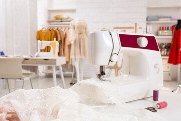 Modern sewing machine with fabric on table in dressmaking workshop
