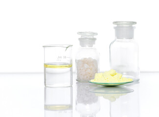 Closeup chemical ingredient on white laboratory table. Sulfur Powder in Chemical Watch Glass place next to oil in Beaker and Flake salt in Chemical Reagent Bottle Glass. Side View