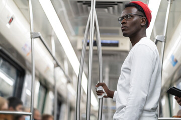 Serious millennial African American man in red hat wear eyeglasses holding handrail with napkin in...
