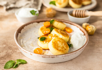 Fototapeta na wymiar Curd or ricotta fritters with physalis, honey, yogurt and mint on a ceramic plate. Cottage cheese pancakes or syrniki. Healthy and tasty breakfast.