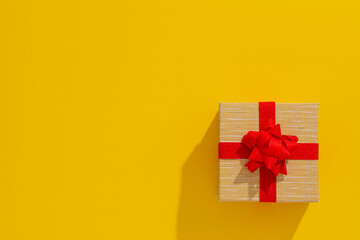 One grey gift box with Red sparkle ribbon and bow on yellow table background. Minimal festive gift background. Top view. Flat lay.	