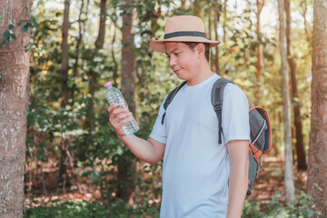 A male tourist carrying a handbag, water bottle and camera walks through the forest.