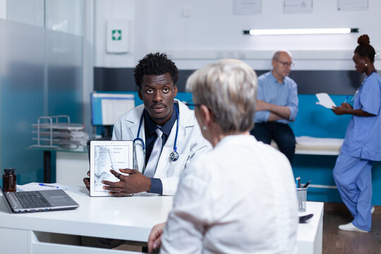 Healthcare Facility General Practitioner Presenting Medical Diagram To Senior Patient. Clinic Specialist Talking With Retired Woman About Health Risks And Clinical Problems While Showing Expertise