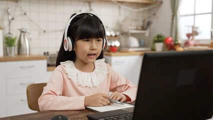 Taiwanese girl with headphones waving hi at computer screen and having conversation with teacher...