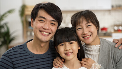 headshot portrait of beautiful asian family of three embracing each other and looking at camera with smile at home.
