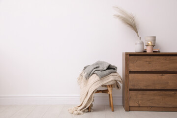 Modern chest of drawers and stool near white wall in room. Space for text