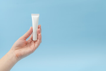 Woman's hand holds white plastic tubes on blue background. Сosmetic bottles for beauty or medicine products