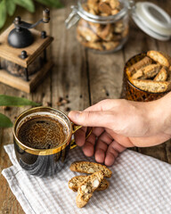 Top view of black coffee with Italian bakery cantuccini with almond over wood brown background, human hand