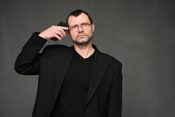 Caucasian middle-aged business man in glasses and a black jacket looks at the camera in displeasure with a smartphone to his head
