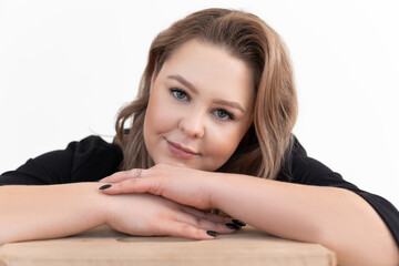 Obraz premium Smiling middle-aged plump woman with long dark hair wearing black cardigan, sitting at table, putting chin on hands.