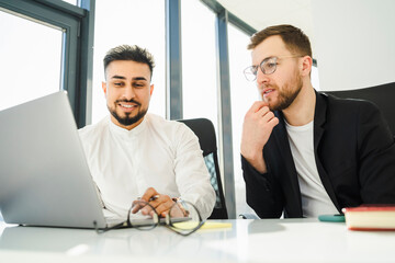 Two office workers are thinking about a new project while sitting at a laptop