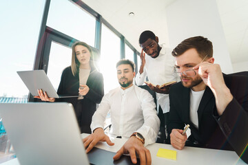 Group of multiracial office workers looking at laptop during meeting in boss's office.