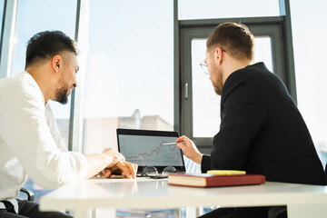 Two businessmen in the office analyze the profit of the company from the graph on the laptop