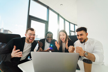 Group of business partners sit in front of a laptop and rejoice in the success of their company
