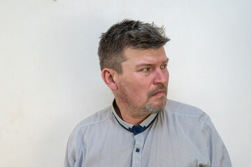 Obraz premium A mature man in a state of psychological stress in front of a light wall. A male with a short haircut and graying hair. People, Human Emotions