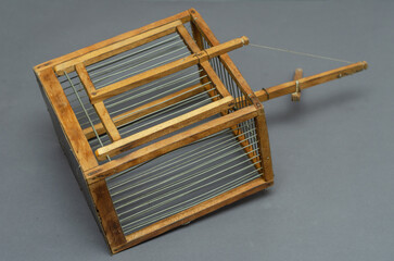 An old wooden trap for catching canaries, chirps, siskins, parrots and other birds on a gray background.