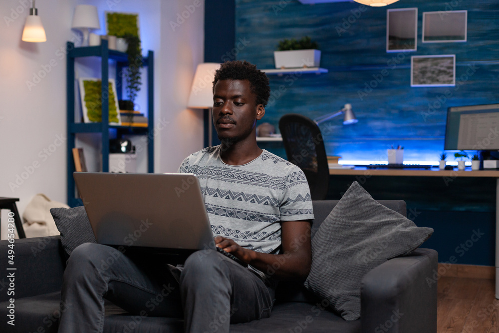 Poster freelancer man resting on sofa holding laptop computer searching financial information working remot