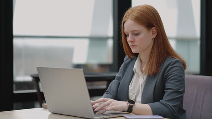 woman is working with laptop in office, typing e-mail for partners and employees, serious and successful businesswoman