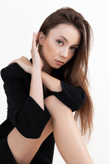 Fototapeta premium Portrait of young slim flawless woman titivating long dark hair, wearing black coat, sitting bending perfect legs.