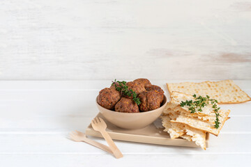 Beef meatballs, fresh thyme and matzah bread for Jewish holiday Pesach or Passover on beige plate over wooden background with copy space.