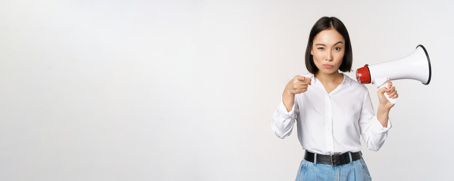 Image of modern asian woman with megaphone, pointing at you camera, making announcement, white background