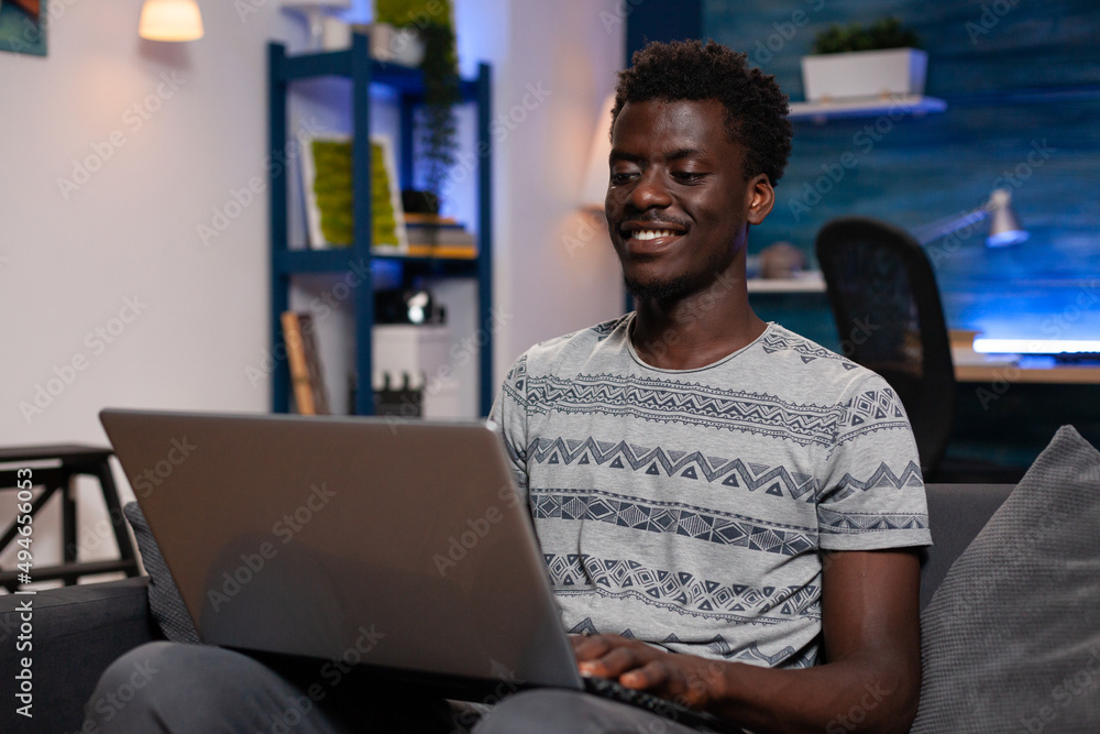 Poster student man sitting on couch holding laptop computer searching financial information working remote 