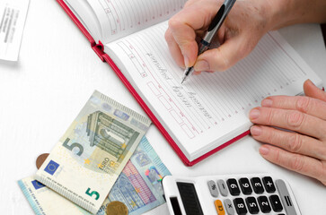 Close-up of the hands of an elderly woman holding a pen working on a utility bill calculator.