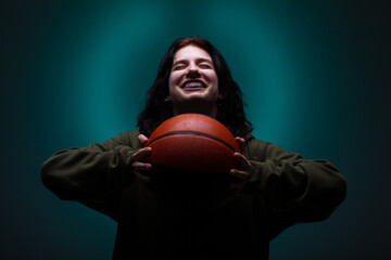 Teenage girl with dental braces holding basketball. Studio portrait on neon blue colored background.. - obrazy, fototapety, plakaty