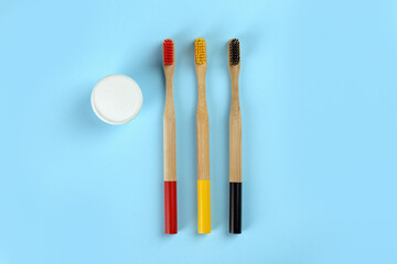 Bamboo toothbrushes and bowl of baking soda on light blue background, flat lay