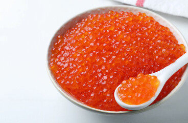 Bowl and spoon with delicious red caviar on white table, closeup