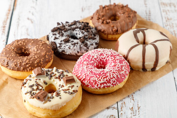 Set of assorted colorful white and dark chocolate glazed donuts with mixed sprinkles on paper on wooden table.
