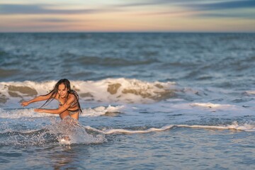 A girl with loose hair walks on the sea with waves and enjoys the sun