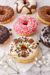 Set of assorted colorful white and dark chocolate glazed donuts with mixed sprinkles on paper closeup on stone table.