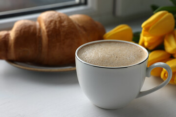 Delicious morning coffee, croissant and flowers near window, closeup