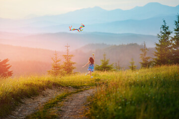 Little happy child girl running with kite. Wonderful mountain landscape in Alps at sunset. Blue ridges of mountains on horizon.