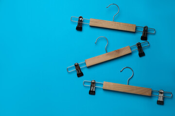 Empty wooden hangers with clips on light blue background, flat lay. Space for text