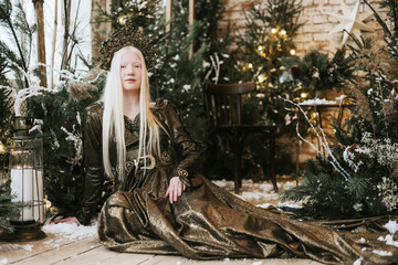 young albino woman with blue eyes and long white hair in beautiful green dress and crown stands in...