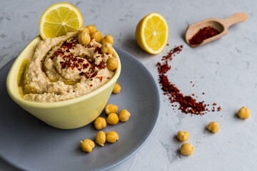 Close-up shot of traditional arabic, israel, turkish food hummus in yellow bowl with chickpeas, leamons and red chili pepper in wooden spatula. Selective focus.