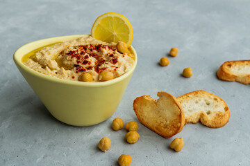 Close-up of traditional arabic, israel, turkish food hummus in yellow bowl with chickpeas, leamons and red chilli pepper and roasted toasts. Selective focus.