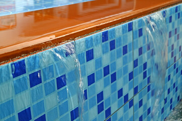 Closeup overflowing water of golden brown and vibrant blue tiled swimming pool spillway